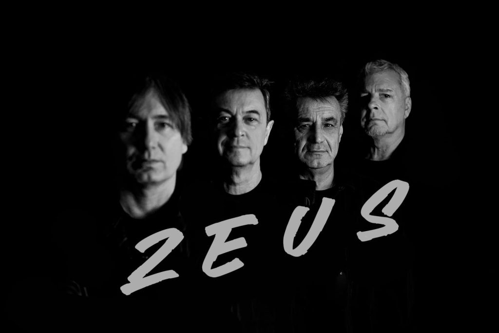 Štyria hudobníci stoja v tmavom prostredí s výrazným tieňovaním tvárí, pred nimi je veľký nápis ZEUS.