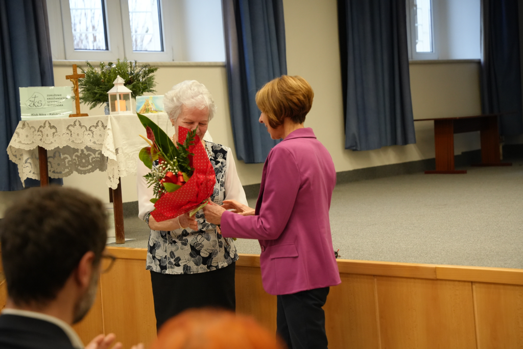 žena odovzdáva kyticu seniorke