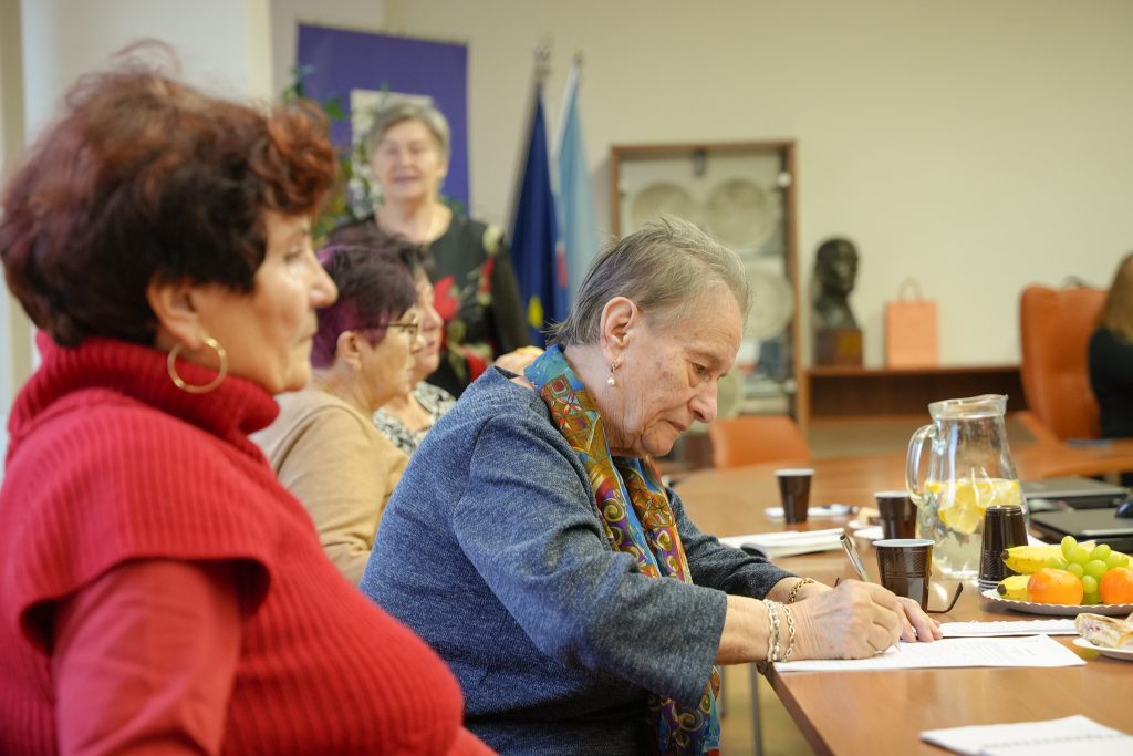 dve seniorky v popredi a dve vzadu sedia na zasadnutí