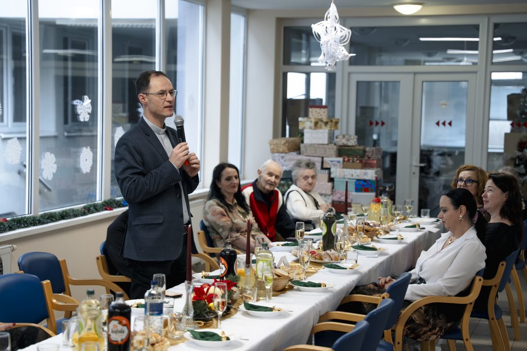 Muž prihovárajúci sa seniorom počas vianočného stretnutia v zariadení sociálnych služieb.