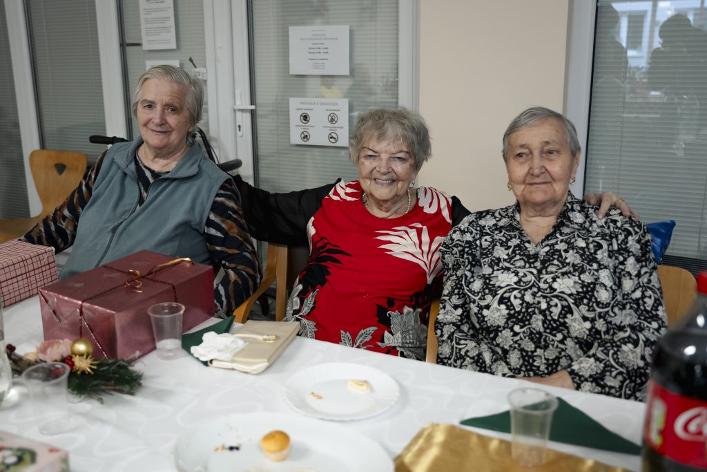 Tri usmiate seniorky sediace pri slávnostne prestretom stole.